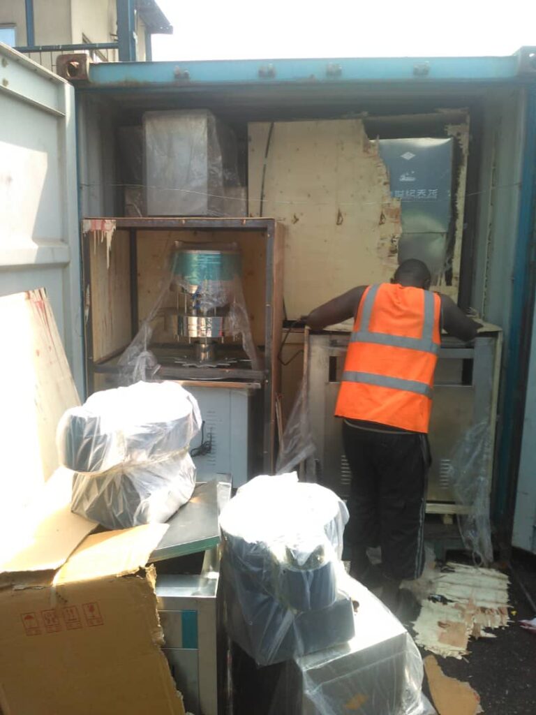 Worker in safety vest unpacking industrial machinery equipment inside a shipping container.