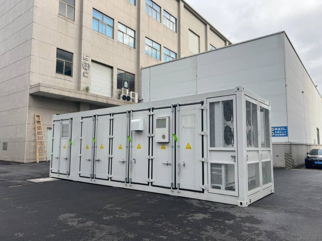 Large industrial modular energy storage container unit parked outside a commercial facility building.