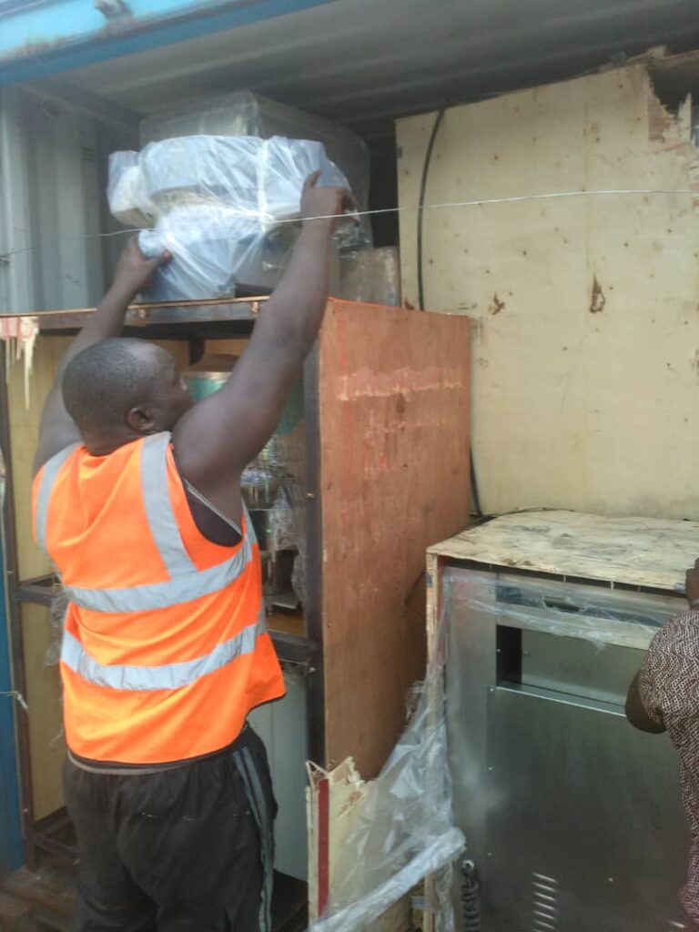 Worker wearing safety vest lifting wrapped industrial equipment inside a shipping container.
