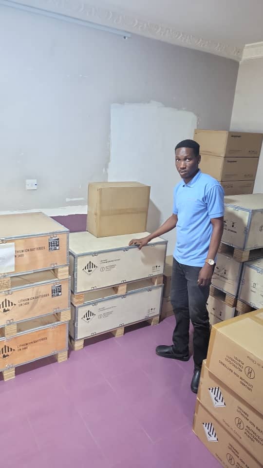 Man standing beside stacked wooden crates labeled lithium ion batteries inside storage warehouse.