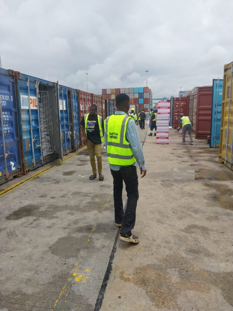 Workers in safety vests inspecting shipping containers at a port yard.